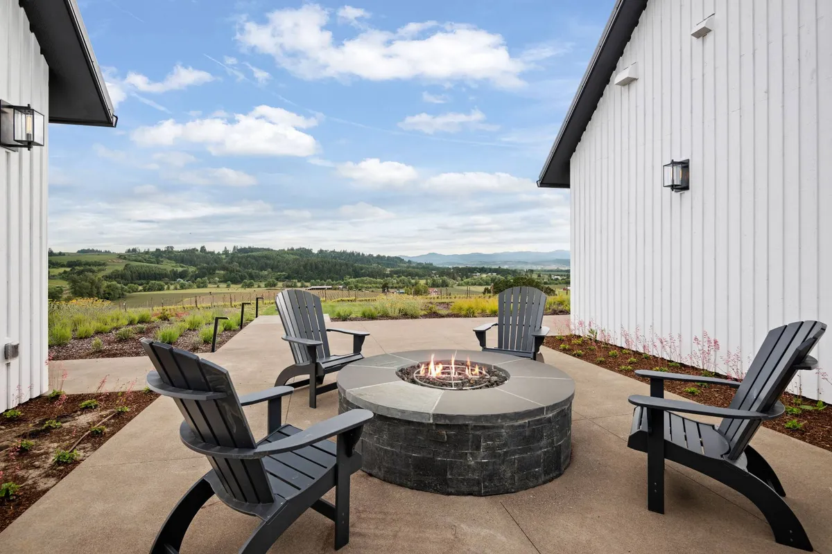 An inviting fire pit area is surrounded by comfortable chairs, with a scenic landscape unfolding beyond. The space is perfect for evening gatherings, storytelling, and stargazing, creating a cozy focal point for social connection.
