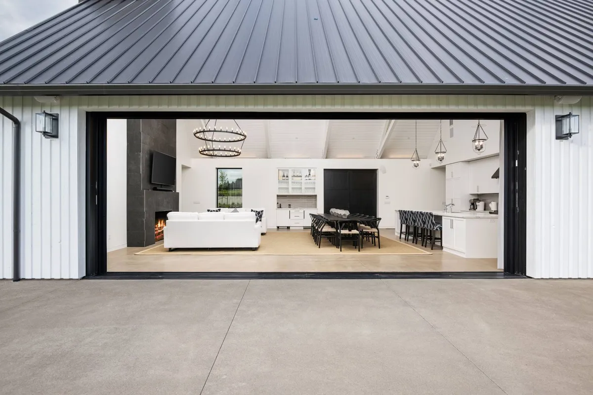 A large, open-plan interior with a white sofa, spacious dining table, and a striking black feature wall. Pendant lights and a modern fireplace add style, while the layout signals customizable seating for different occasions.