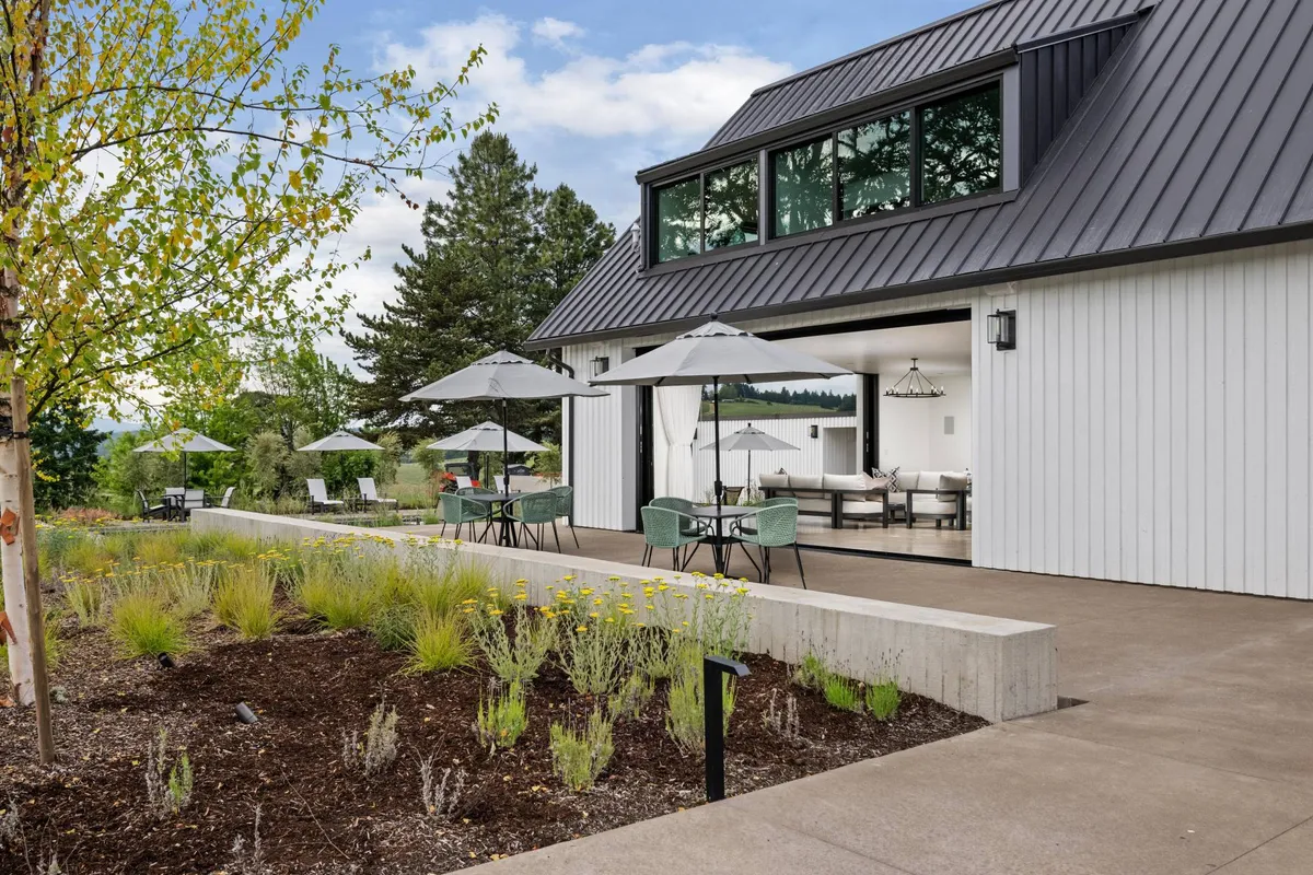 A wide exterior view of the estate’s modern architecture, highlighted by an elegant outdoor seating area with umbrellas. The lush landscaped garden surrounds the space, creating a peaceful, secluded setting ideal for group dining, sunset dinners, or relaxed celebrations. The inviting arrangement connects the home seamlessly with the outdoors.
