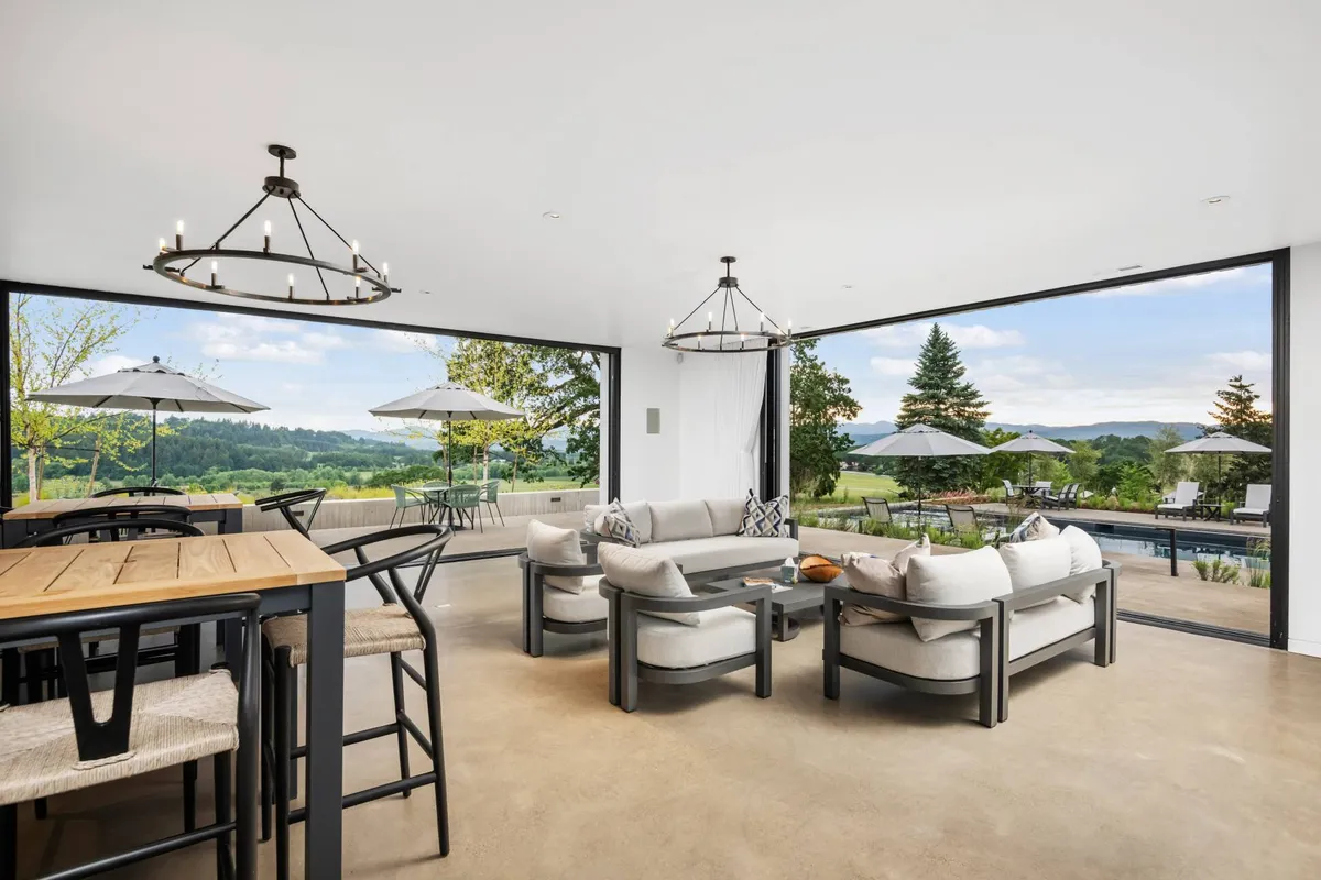 A spacious, open-concept living and dining area filled with natural light. Large windows frame spectacular valley views, while modern furniture and elegant chandeliers create a comfortable, luxurious ambiance. The seamless connection to the outdoors is evident, with the space designed for both relaxation and lively gatherings.
